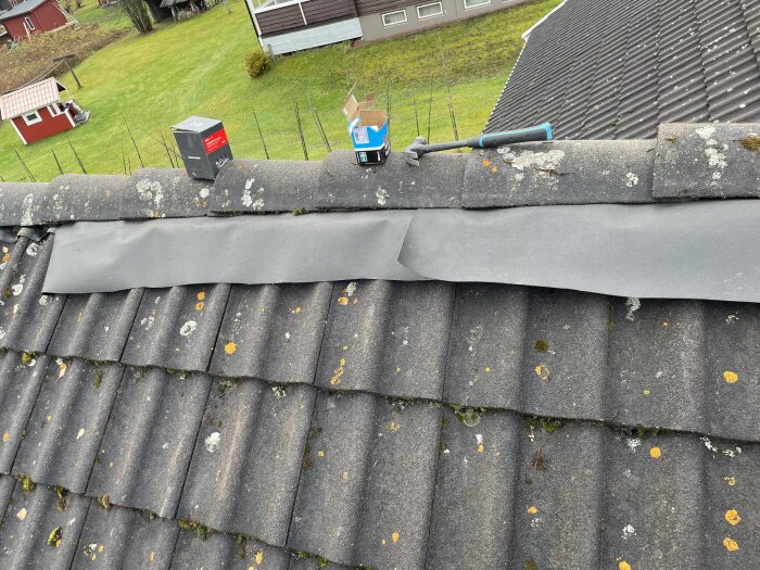 Tak med lösa nockpannor, underlagsduk fastsatt över nocken; taklagningsmaterial och hammare syns ovanpå.