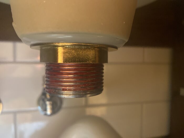 Nära bild av ett rörgäng med röd VVS-tätning applicerat, ovanför en vit porslinshandfat.