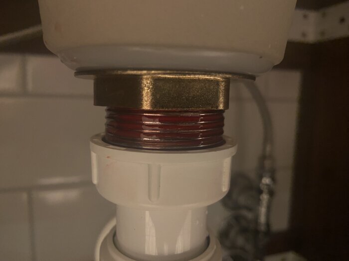 Närbild av röranslutning under diskbänk med röd VVS-tätning applicerad på gängorna.