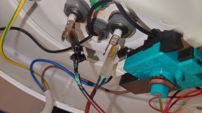 Närbild av elektrisk anslutning med brända och svarta kablar, lossnade ledare och plastdelar i en vattenvärmare.