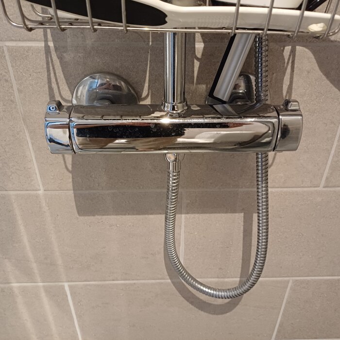 Nära bild på duschblandare från FM Mattsson med vred för temperatur och val mellan tak- och handdusch. Grå kakel som bakgrund.