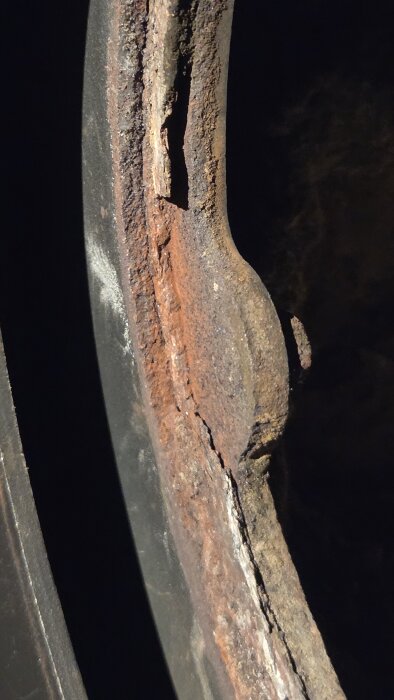 Närbild av rostig kant på en rund täckplåt inne i en kamin, delvis täckt med sot och smuts.