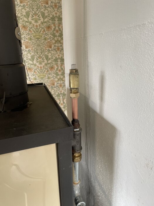 Ett 15mm kopparrör med kopplingar anslutet till en värmepump, beläget intill en blommig tapet, del av ett hemmaprojekt.