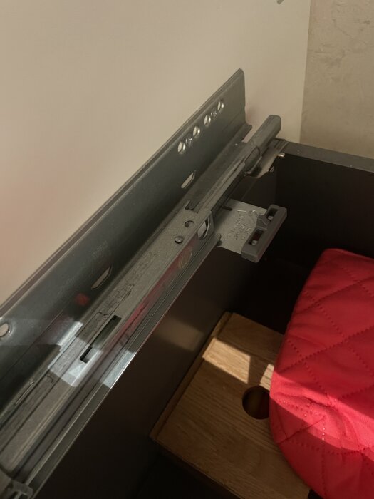 Push open-lådmekanism med synlig justeringsdel och röd kudde i bakgrunden i badrumslåda.
