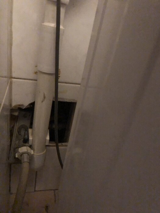Avloppsrör och VVS-installation i ett badrum, delvis dolda bakom en panel. Problem med dålig lukt beskrivs i inlägget.