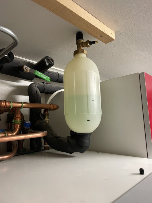 En expansionskärl med ventil monterad i ett värmesystem med kopparrör och isolering i ett teknikutrymme.