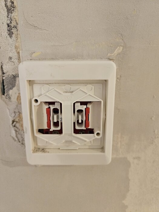 Väggmonterat eluttag med plastram men utan knapp, på obehandlad vägg; frågeställaren vill ta bort ramen.