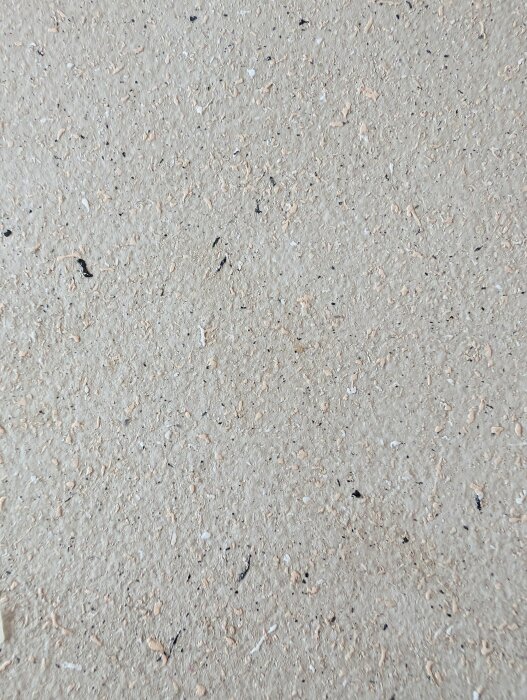 Bild av en bordsyta med ojämn struktur i beige nyans, potentiellt sprayad spånskiva, med små mörka fläckar.