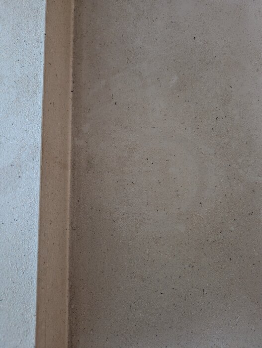Närbild av en bordsytas hörn med fläckar, potentiellt sprayad spånskiva, visar textur och renoveringsbehov.