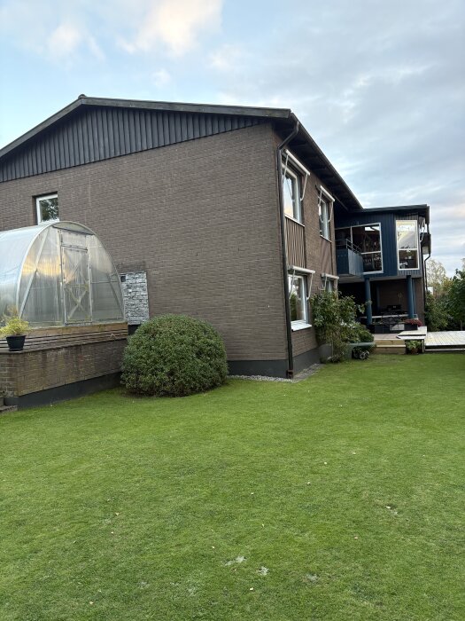 Suturängvilla med målad tegelfasad, gräsmatta och växthus i bakgrunden.