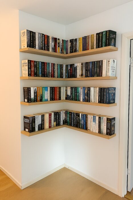 Hörnhyllor fulla med böcker mot en ljus vägg. Trelagers hyllsystem monterat i hörnet, med flera böcker på varje hylla.
