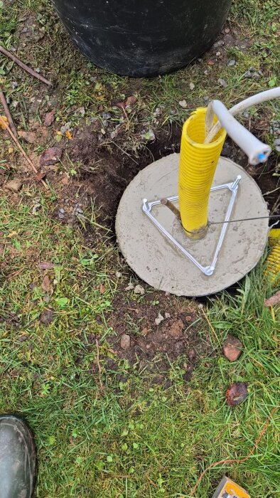 En gul kabel i ett betongfundament på gräsmark för montering av stolplykta.