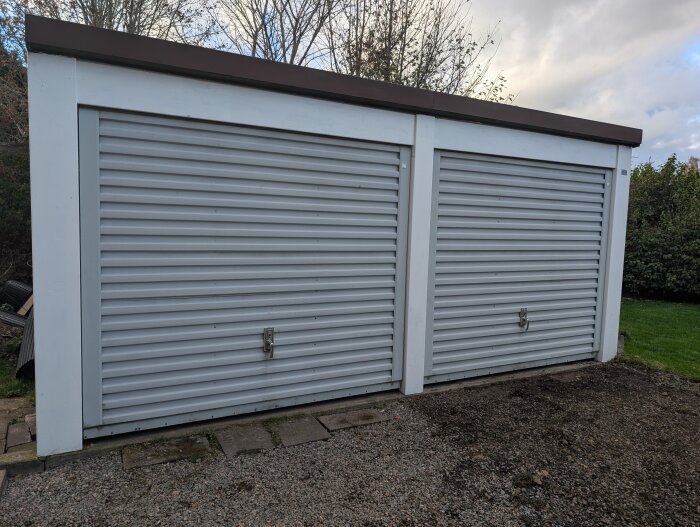 Dubbelgarage med plåtfasad och eternittak från 1969, sett framifrån med stängda garageportar och omgivande grönska.