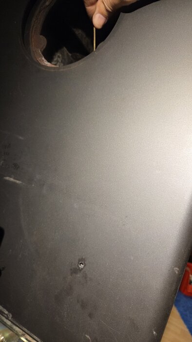 Person håller en plåt med ett runt urtag och hål, förberedd för montering med ny skruv efter att ha fastnat i pellets mataren.