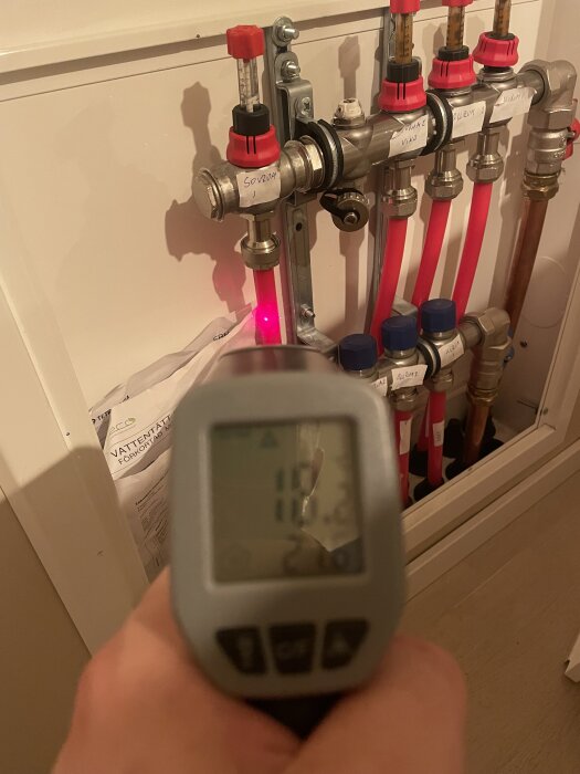 Golvfördelare med flödesmätare och flera rör, en hand håller en termometer som visar 19 grader.