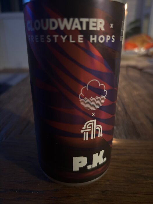 En ölburk med texten Cloudwater Freestyle Hops och logotyper, stående på ett träbord.