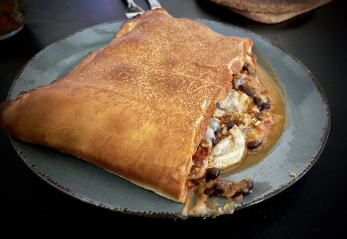 Inbakad pizza eller pirog fylld med chili con carne, tomatsås, ost och skivad lök på en tallrik.