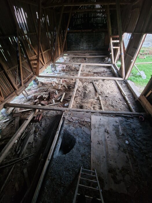 Renovering av logens golv med utspridda brädor och grus, arbetsmaterial och verktyg synliga. Dagljus strömmar in genom träväggarna.