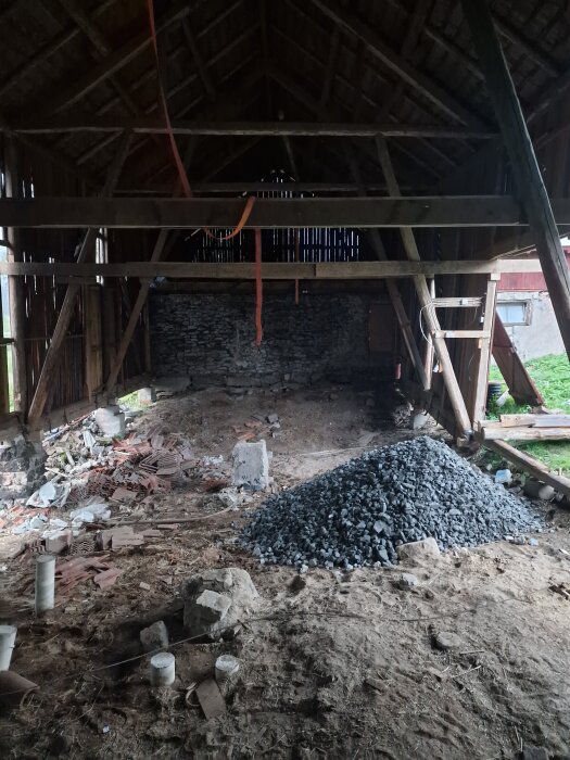 Renovering av loge med högt tak, synliga bjälkar, grushög i mitten, staplade tegelstenar och en stege mot väggen.