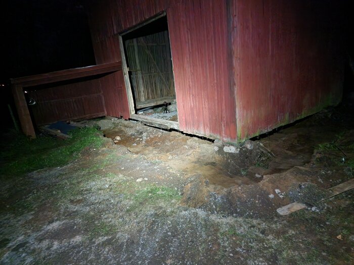 Renovering av logens grund med synlig jord och rödfärgad fasad i mörker.