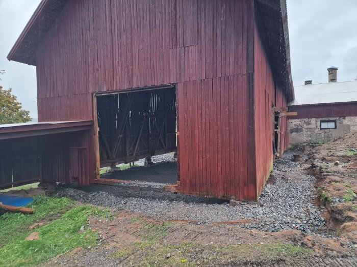 Röd träloge under renovering med öppen del och grusmark runt om, förberedd för gjutning och byggarbeten.
