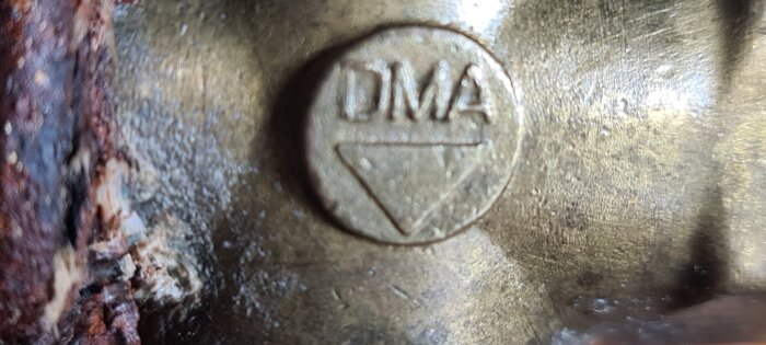 Närbild av en mässingsventil märkt "DMA" med rostig yta, del av värmeledningssystem i källare, läcka vid vredet, från hus byggt 1970.