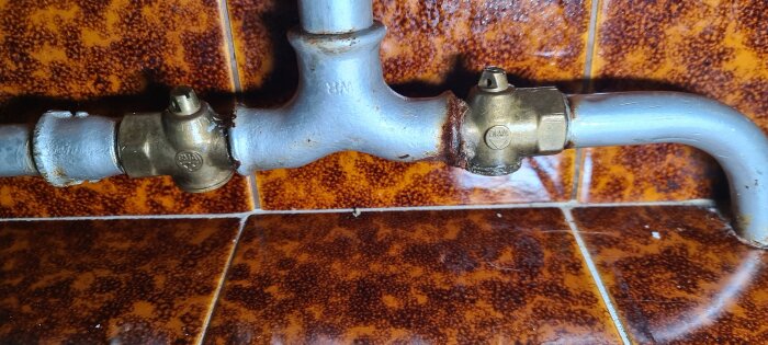 Rörsystem med kopplingar och ventiler i källaren, där vissa delar uppvisar läckage vid vredet, över tegelmönstrat golv.