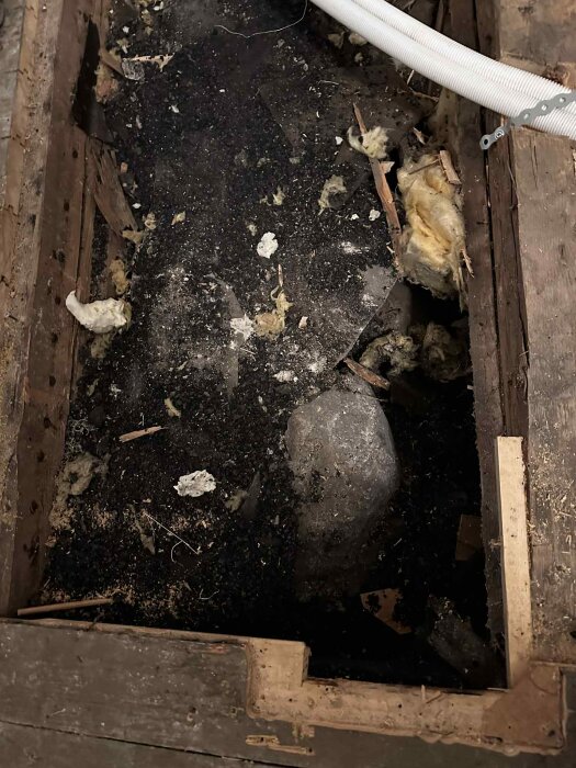 Öppet golv med synlig krypgrund fylld med koks och sten; rester av trä och isolering synliga.