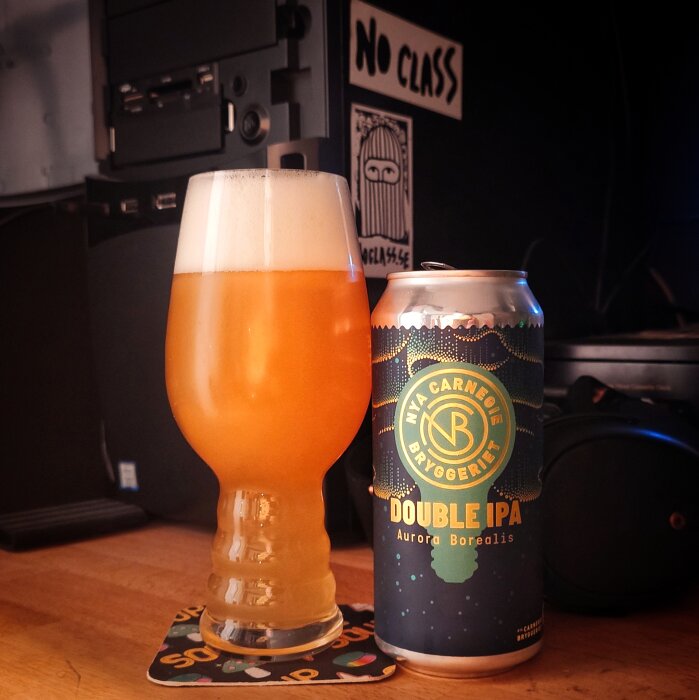 Ölglas med skummig IPA bredvid en burk Double IPA från Nya Carnegie Bryggeriet på ett bord.