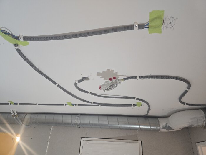 Tak med eldragningar, spirorör och gröna tejpbitar förberedda för gipsning vid ett renoveringsprojekt i en källarkorridor.