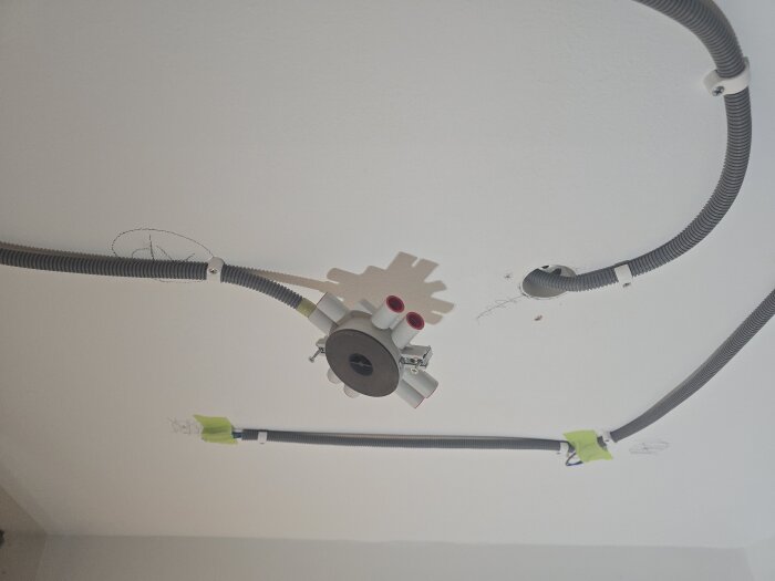 Elektrisk installation i vitt tak med kabelrör och en dosa, förberett för gipsning. Grön tejp används vid eltrådarna.