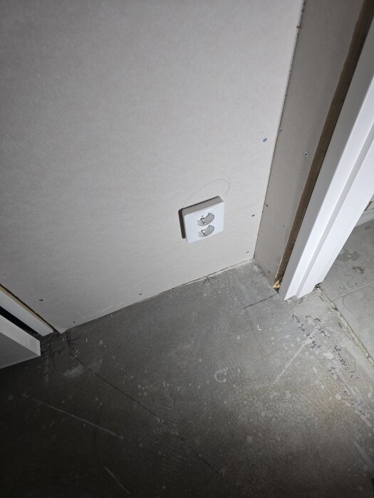 Vägg med fastsatt nätverksuttag och betonggolv i ett rum under renovering, gipsad vägg synlig, dörrkarm vid sidan.