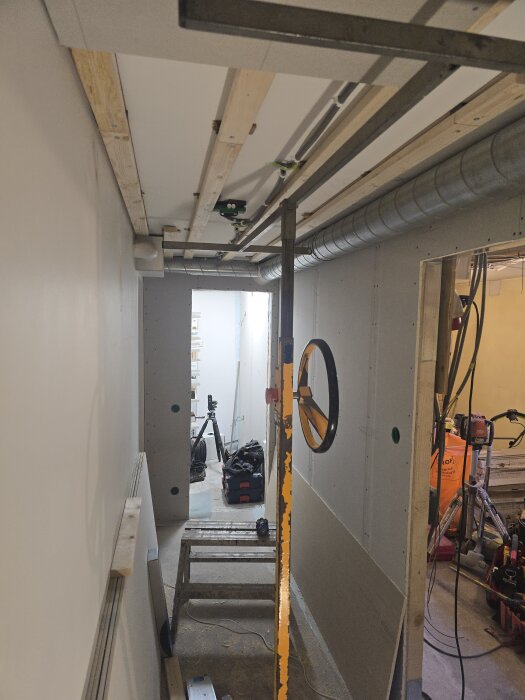 Renovering av källarkorridor med gipsinstallation, synliga ventilationsrör och byggutrustning i bakgrunden.