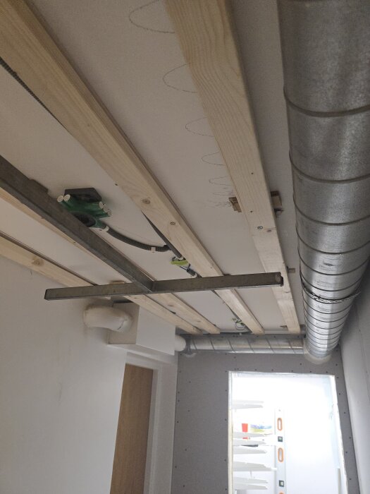 Källarkorridor med montering av gipstak, synliga träbalkar, elkablar och metallrör, förberedelser innan taket täcks med gips av snickare.