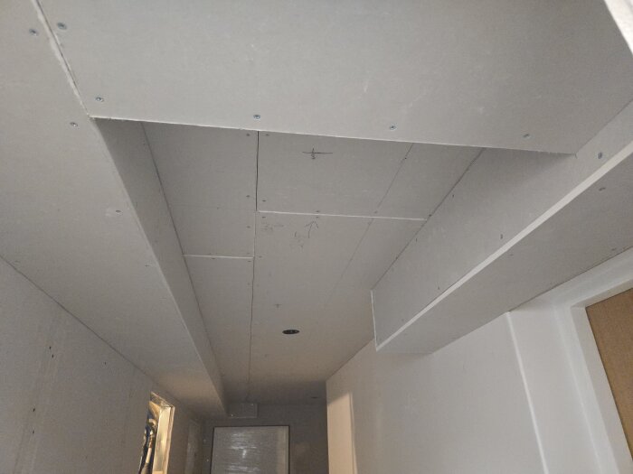 Nygipsat tak och väggar i en källarkorridor med monterade takdosor, visat före målarens och golvläggarens arbete.