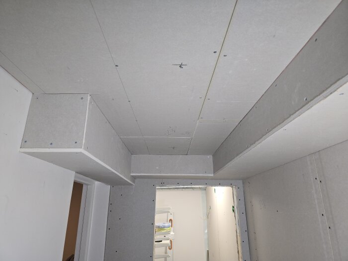 Gipsskivor monterade i tak och väggar i en källarkorridor, med synliga skruvar och olika nivåer för att anpassa till byggprojektets krav.