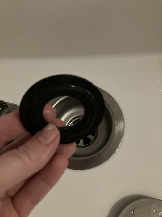 Hand håller en svart packning över en diskbänk.