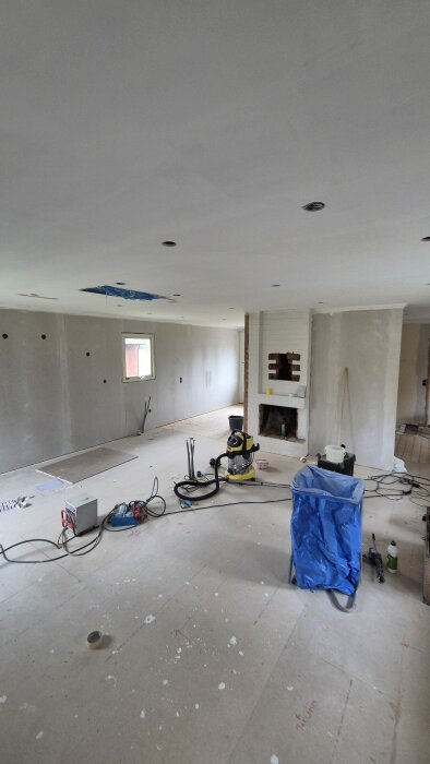 Renoverat rum med målat tak, väggar med hål för ventilation och en öppen spis. Verktyg och utrustning utspridda på golvet.