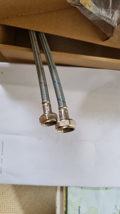 Två flätade slangar med metallkopplingar för diskmaskinsanslutning, avstängning märkta med röd och blå färg.