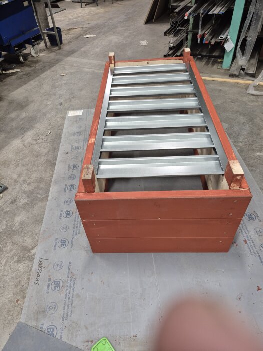 Byggprojekt med en låda av rödmålat trä och botten av plåt i en verkstadsmiljö.