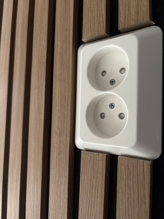 Vägguttag monterat mellan träribbor på en vägg.