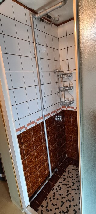 Rörinstallation längs duschväggen med våta ytor från WD-40, omgiven av vita och bruna kakelplattor i ett badrum.