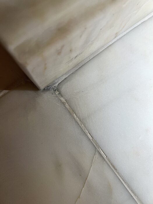 Marmorgolv med repor och synliga ådringar. Djupa repor och rundade kanter syns, med smuts innesluten i ådringarna efter felaktig slipning.