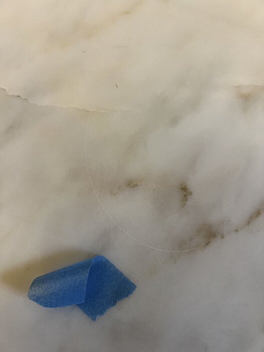 Marmor med repor och virvlar, blå tejp på ytan, smuts i ådring synlig.