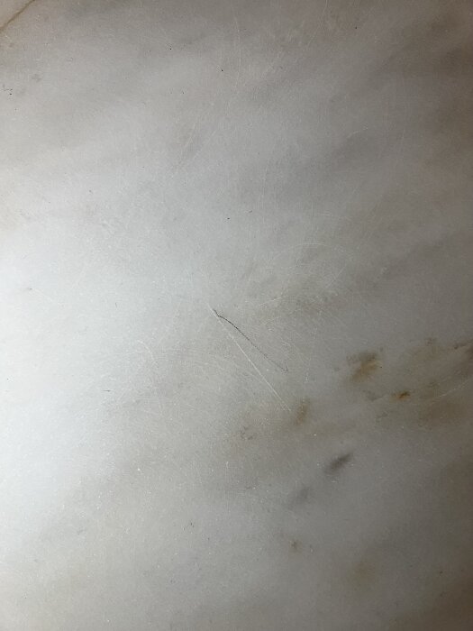 Marmoryta med repor och virvlar, synligt smuts och djupare ådring efter slipning. Tecken på misslyckat försök att jämna ut ytan.