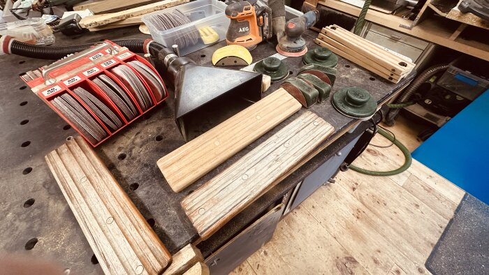 Verktygsbänk med slippapper, trädelar och slipklossar för restaurering av båtens teakdetaljer i ett snickeri.