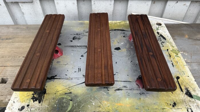 Tre slipade teakträlister på en arbetsbänk, målade med mörk finish.