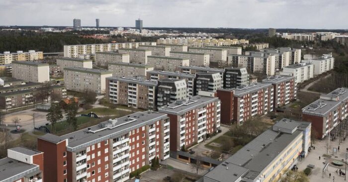 Flygfoto av ett modernistiskt bostadsområde med flera rader av flerbostadshus och omgivande grönområden i en förortsmiljö.