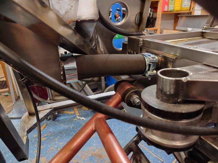 En monterad slang med två klämmor på en metallstruktur, omgiven av olika metall- och plastkomponenter i ett garage.