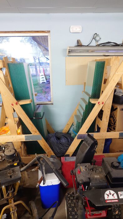 Glasrutor staplade i träställning i garage, med trädgårdsutrustning och kablar omkring. Söker metoder för att skilja ihopklistrade glasrutor.